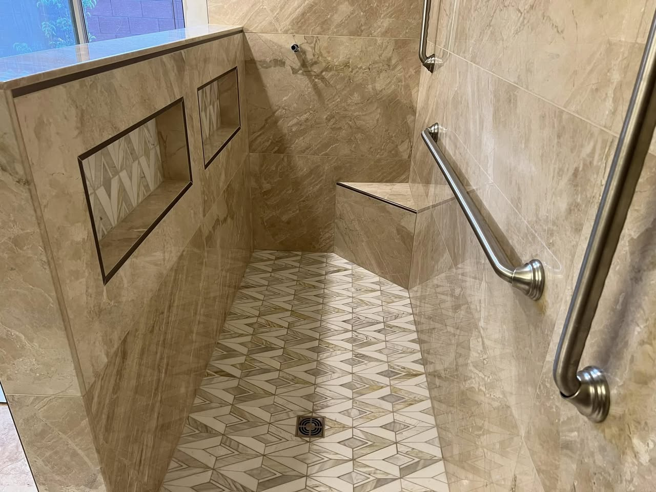 Marble walk-in shower with bench, recessed niches, and geometric mosaic floor
