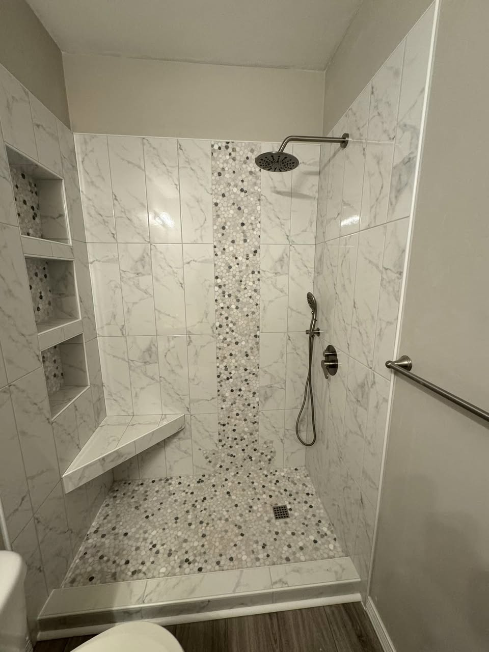Marble-look custom shower with pebble mosaic feature strip, bench seat, and triple recessed niches