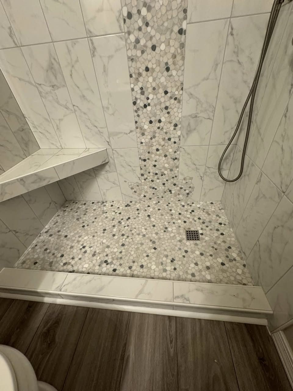 Pebble mosaic shower floor with marble-look wall tile and built-in bench