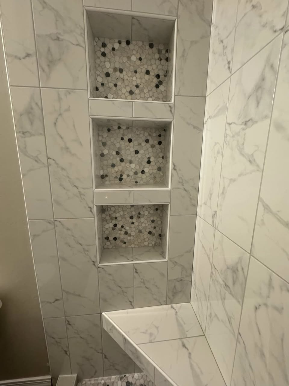 Three stacked shower niches with pebble mosaic accents and marble-look tile