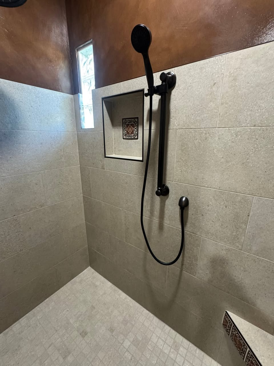 Walk-in shower with stone-look tile, recessed niche and oil-rubbed bronze fixtures