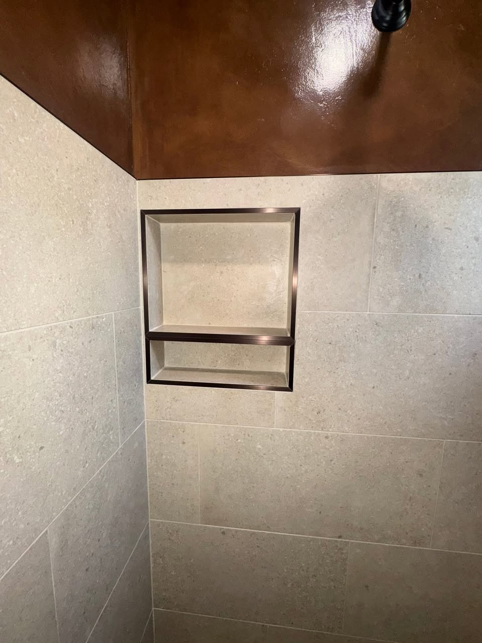Double shower niche with bronze trim and stone-look porcelain tile
